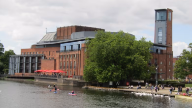 The Royal Shakespeare Theatre and its tower seen across the River Avon in Stratford-upon-Avon, with rowing boats on the river
